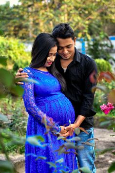 a pregnant couple cuddles in the middle of a garden while holding each other