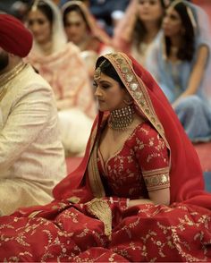 a woman in a red bridal gown sitting on the floor with other people behind her