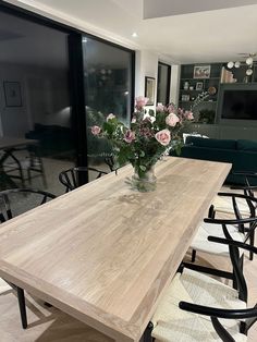 a wooden table with chairs around it and flowers in a vase on the table top