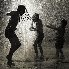 three children playing in a fountain with water spraying from their heads and hands, black and white photograph