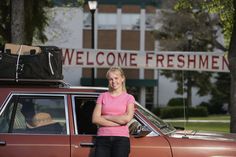 a woman standing in front of a car with luggage on the roof and welcome freshmen sign behind her