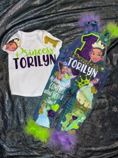 two princesses shirts are laying on top of a bed with purple and green pom - poms