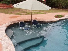 two lawn chairs sitting in the middle of a pool with an umbrella over it and some water