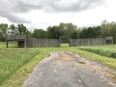 an empty dirt road in the middle of a grassy field with two wooden gates on each side