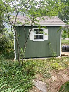 a small green shed sitting in the middle of a yard next to trees and bushes