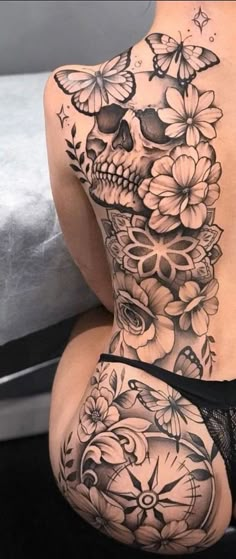 a woman's back tattoo with flowers and skulls on it, as well as butterflies