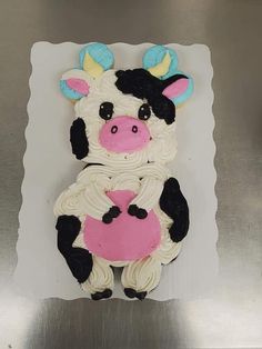 a cake shaped like a cow holding a pink heart on top of a metal surface