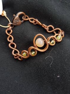 a close up of a bracelet on a black cloth with an orange and white bead