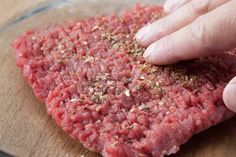 a person touching ground meat on top of a wooden cutting board