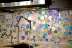 a kitchen sink under a faucet next to a wall covered in colorful circles