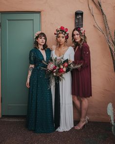 three women standing next to each other in front of a door with flowers on their heads