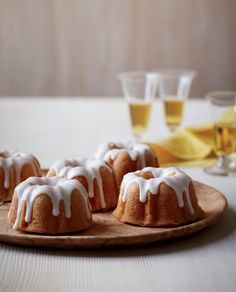 small bundt cakes with icing on a wooden platter next to glasses of wine