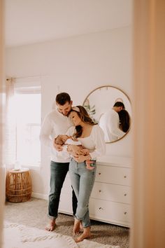 a man and woman standing in front of a mirror holding their newborn son, who is looking at his belly