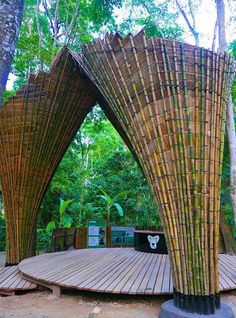 an outdoor bamboo structure in the middle of a forest with trees and benches around it