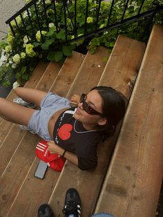 a woman laying on top of a wooden bench next to a flower filled planter