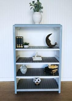 a blue shelf with books, vase and other items on it in front of a white wall