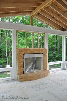 an empty room with a fire place in the center and windows on both sides, surrounded by trees