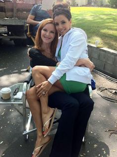 two women sitting on a chair in the middle of a street, one is holding her arm around the other's shoulder