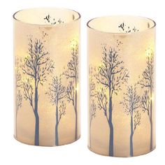 two white candles with trees on them sitting next to each other in front of a white background