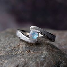 a silver ring with a rainbow colored stone in the middle on top of a rock