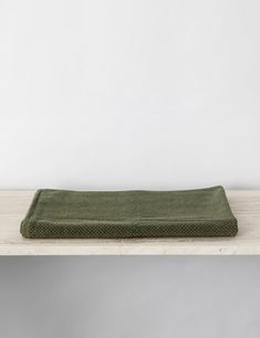 a green towel sitting on top of a wooden shelf in front of a white wall