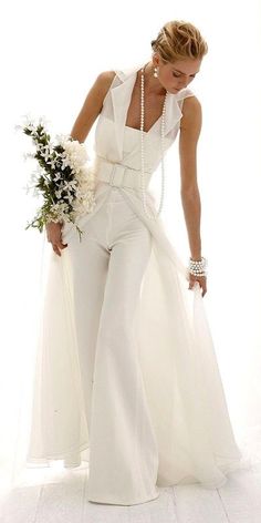 a woman in white is holding a bouquet and posing for the camera with her hands on her hips