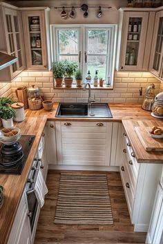 a kitchen with wooden counter tops and white cabinets, along with potted plants on the window sill