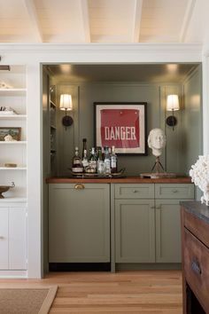 a kitchen with green cabinets and wooden flooring next to a wall mounted sign that reads danger