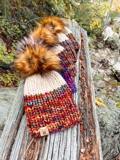 two knitted hats sitting on top of a wooden bench next to trees and rocks