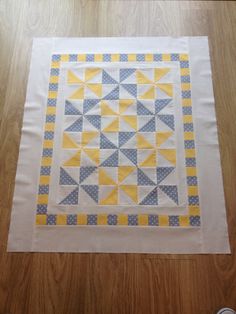 a quilted table runner with yellow and gray triangles on it, sitting on a wooden floor