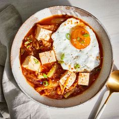 a bowl of soup with tofu and an egg on top, next to a spoon