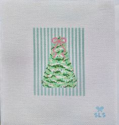 a cross - stitch christmas tree on a white cloth with green and pink stripes in the background