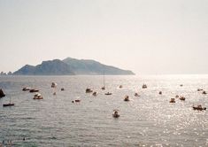 many small boats floating in the ocean on a sunny day with mountains in the background