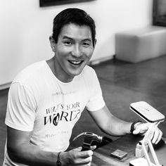 a black and white photo of a man sitting at a table holding a cell phone