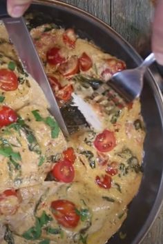 a person cutting into a pizza with tomatoes and spinach on the side, in a pan