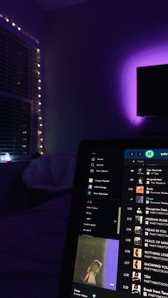 an open laptop computer sitting on top of a bed in front of a purple light