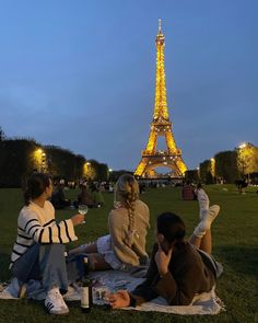 three people sitting on the grass in front of the eiffel tower at night