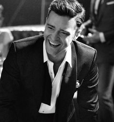 black and white photograph of a smiling man in a suit sitting at a table with other people