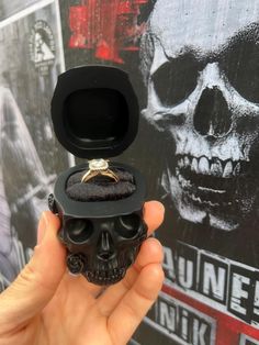 a hand holding a ring with a skull on it in front of a black box