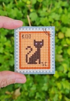 a hand holding up a small cross stitched square with a black cat on it