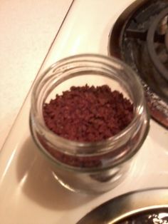 a glass jar filled with red dirt sitting on top of a stove burner next to a frying pan