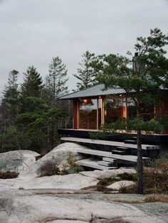 the house is surrounded by trees and rocks, with a deck leading up to it