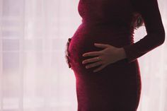 a pregnant woman is standing in front of a window with her hands on her belly