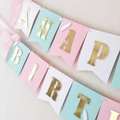 a happy birthday banner with gold letters and pink, blue, and white paper streamers