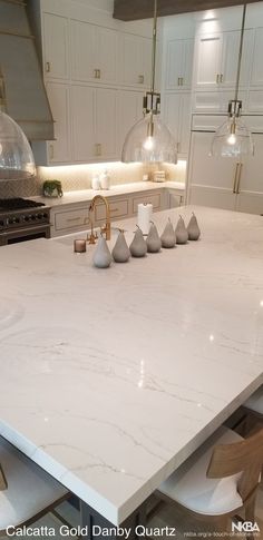 a large kitchen island with white marble countertops and pendant lights hanging from the ceiling