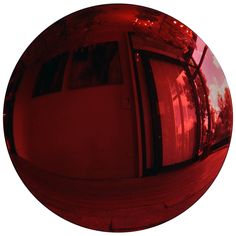 the reflection of trees and buildings in a round red object that appears to be reflecting it's surroundings