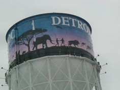 an elephant painted on the side of a water tower with people and elephants walking around