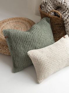 three knitted pillows sitting next to each other on a white surface with a basket in the background