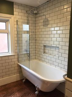 a bath tub sitting next to a window in a bathroom with white tiles on the walls