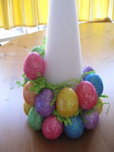 an easter decoration made out of colored eggs on a table with a white pillar in the background